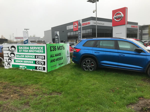 Blue car parked in front of a Nissan dealership with service signs in the foreground.